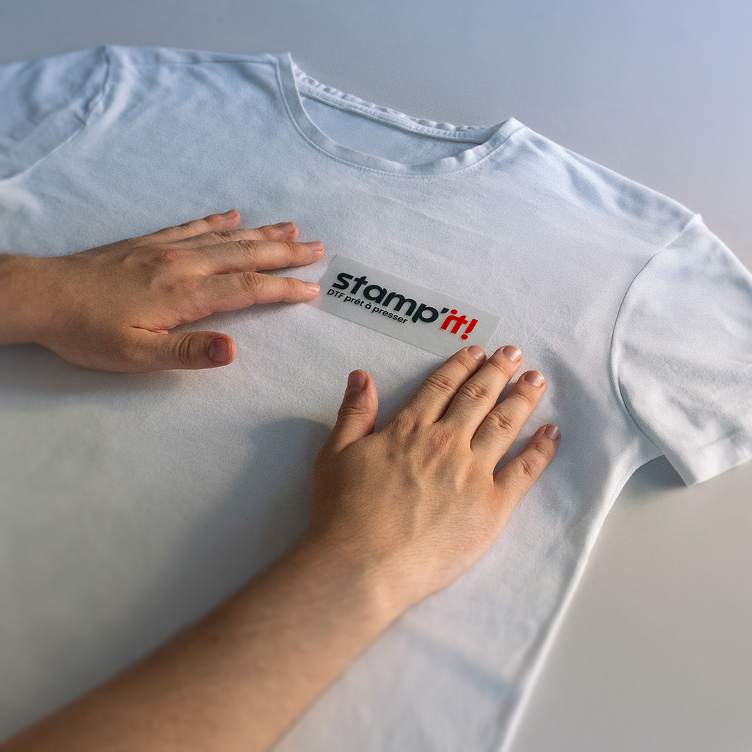 Mains plaçant un petit logo Stamp'it! sur un t-shirt blanc